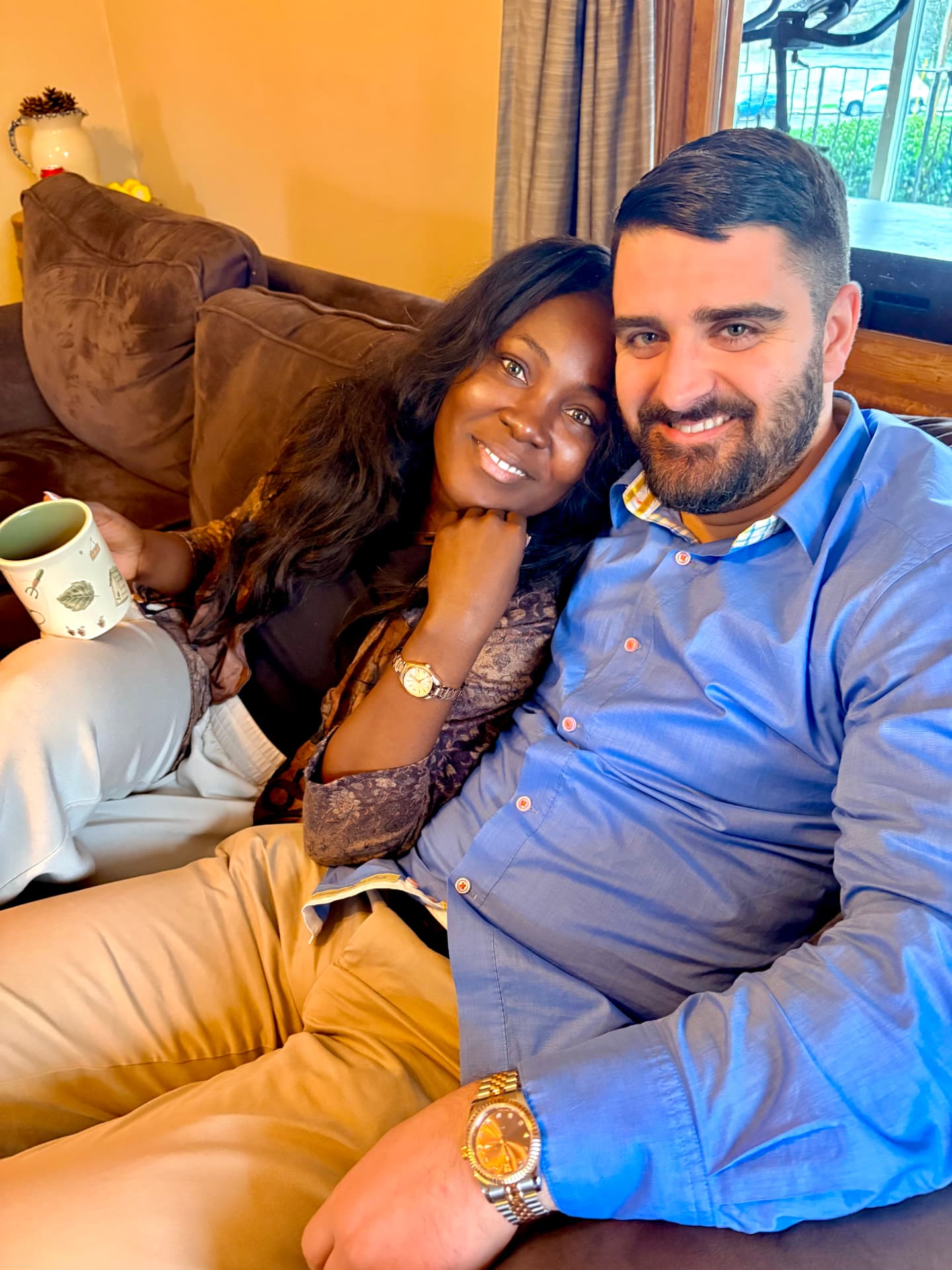 Trish and Trevor smiling together on a sofa, Trish holding a cup of tea